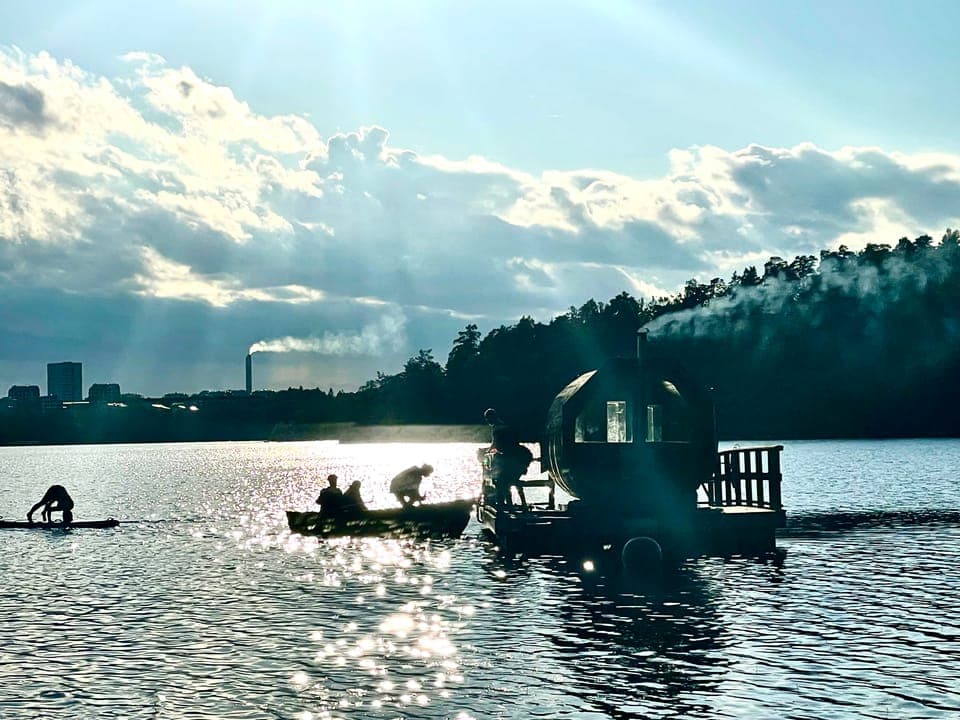 Gäster ror ut till flotten i motljus med stan i bakgrunden
