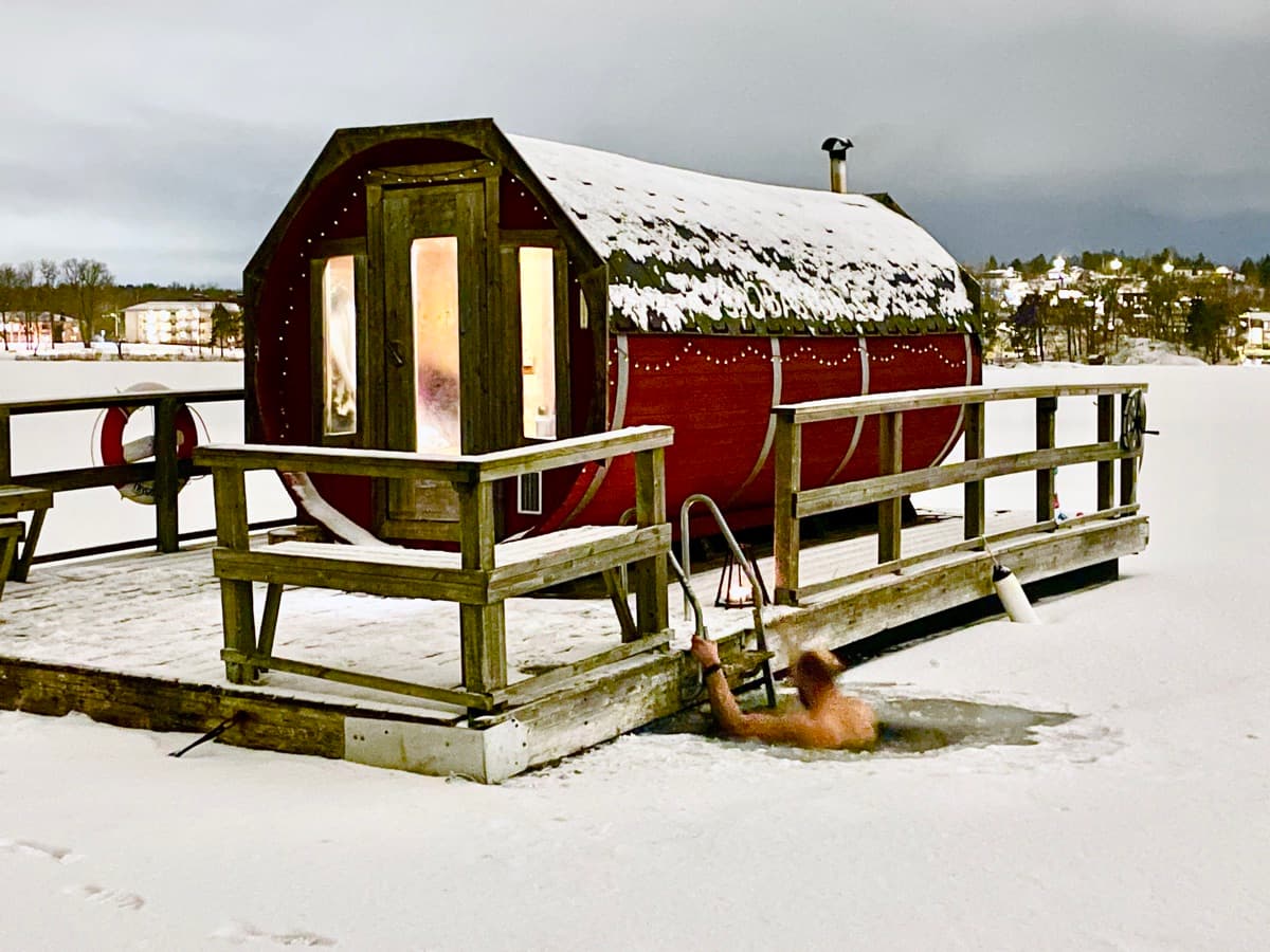 Ett dopp i isvaken vid den upplysta bastuflotten en snöig vinterkväll